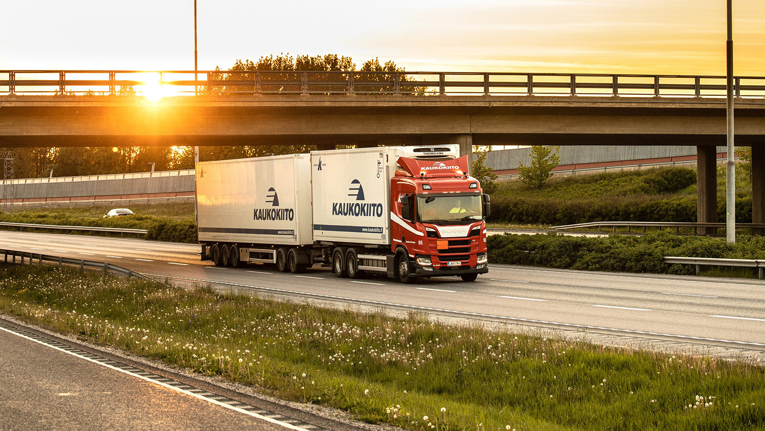 Kaukokiidon rekka-auto ajaa sillan alitse auringon noustessa