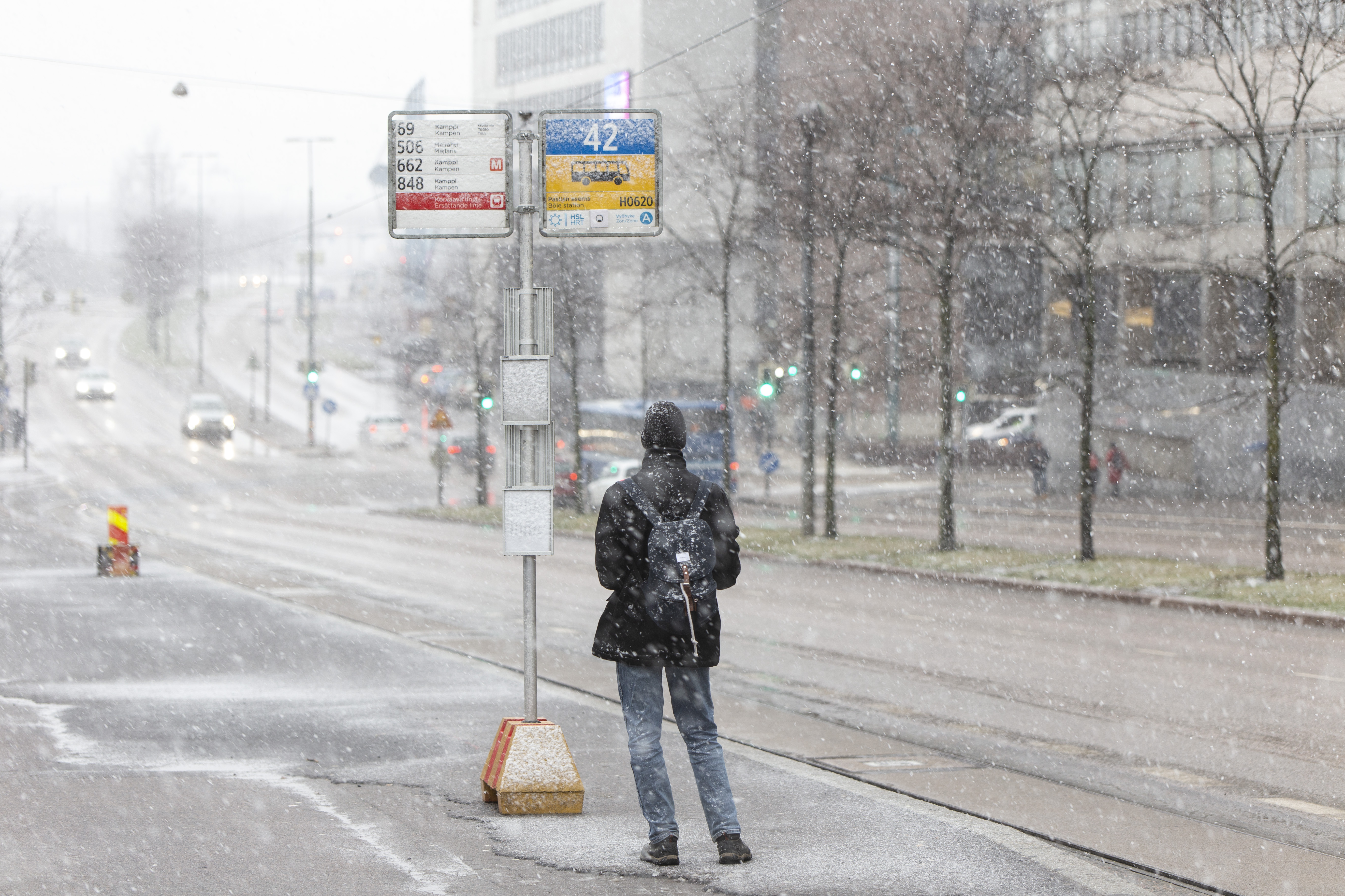 Ihminen pysäkillä lumisateessa