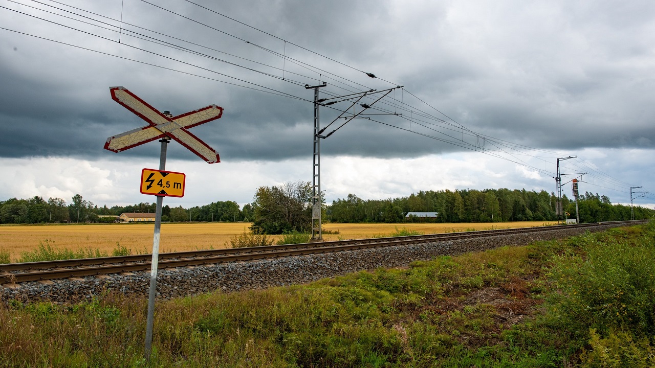 Sähköistetty rata peltojen keskellä, tasoristeys-liikennemerkki etualalla