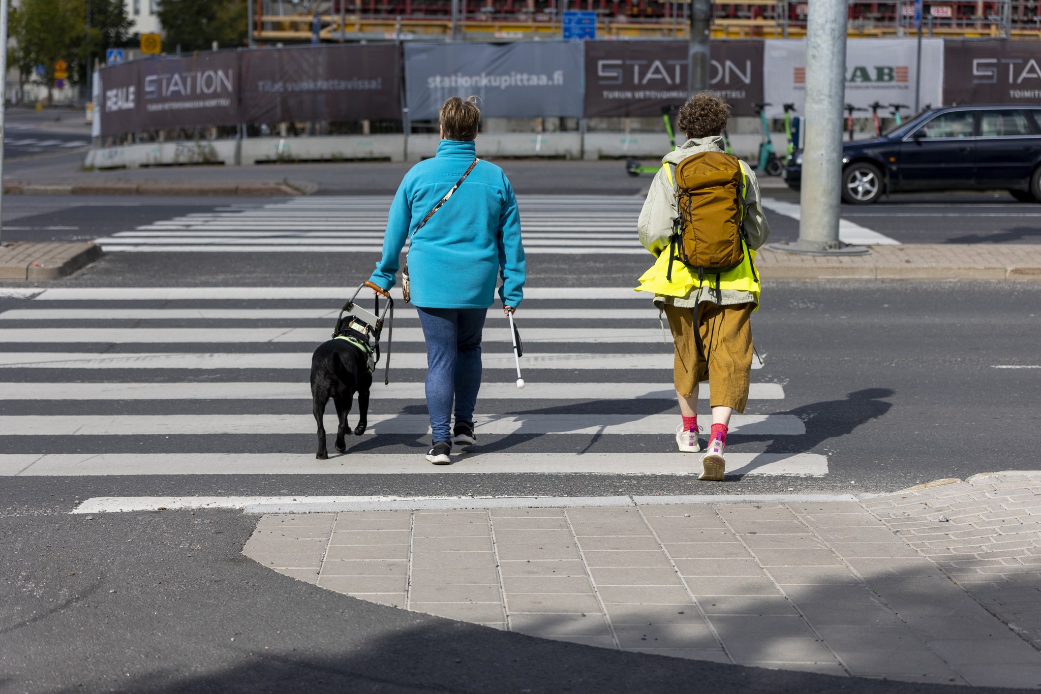 Näkövammainen henkilö kävelee suojatiellä apunaan valkoinen keppi ja opaskoira.