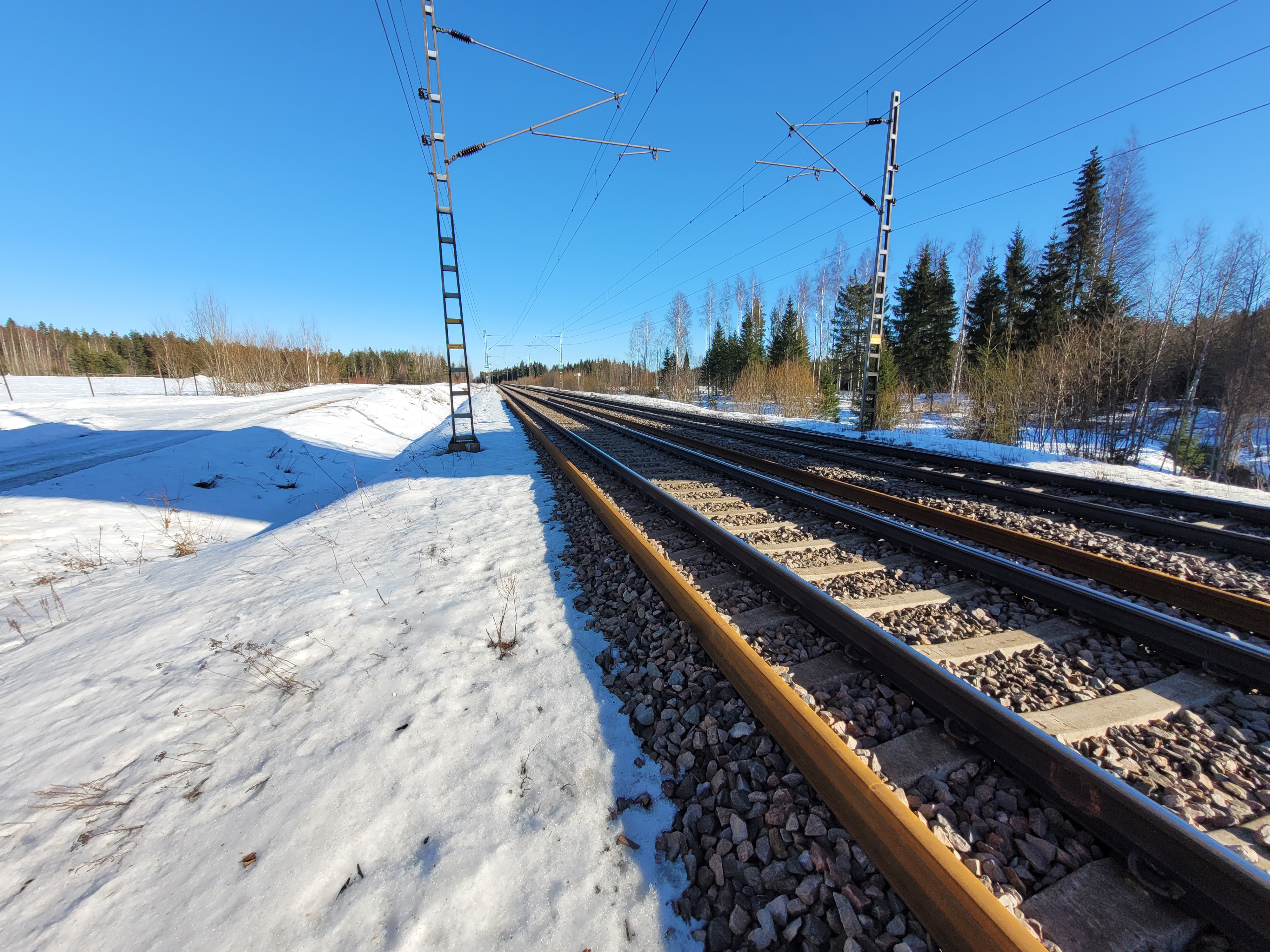 Talvella lunta radan vierellä, takana sähköratapylväitä ja etualalla kiskoja