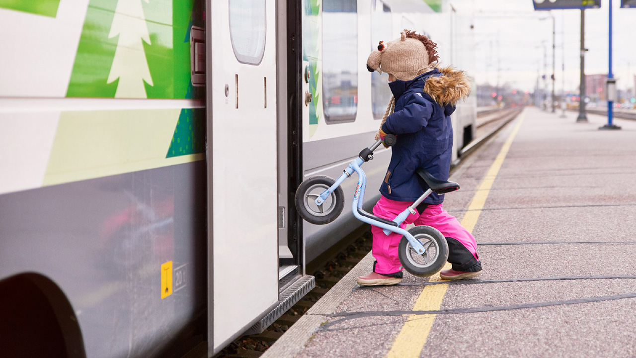 Lapsi nousee asemalaiturilta junaan potkupyörää taluttaen, laituri ja junan lattia ovat samassa tasossa.
