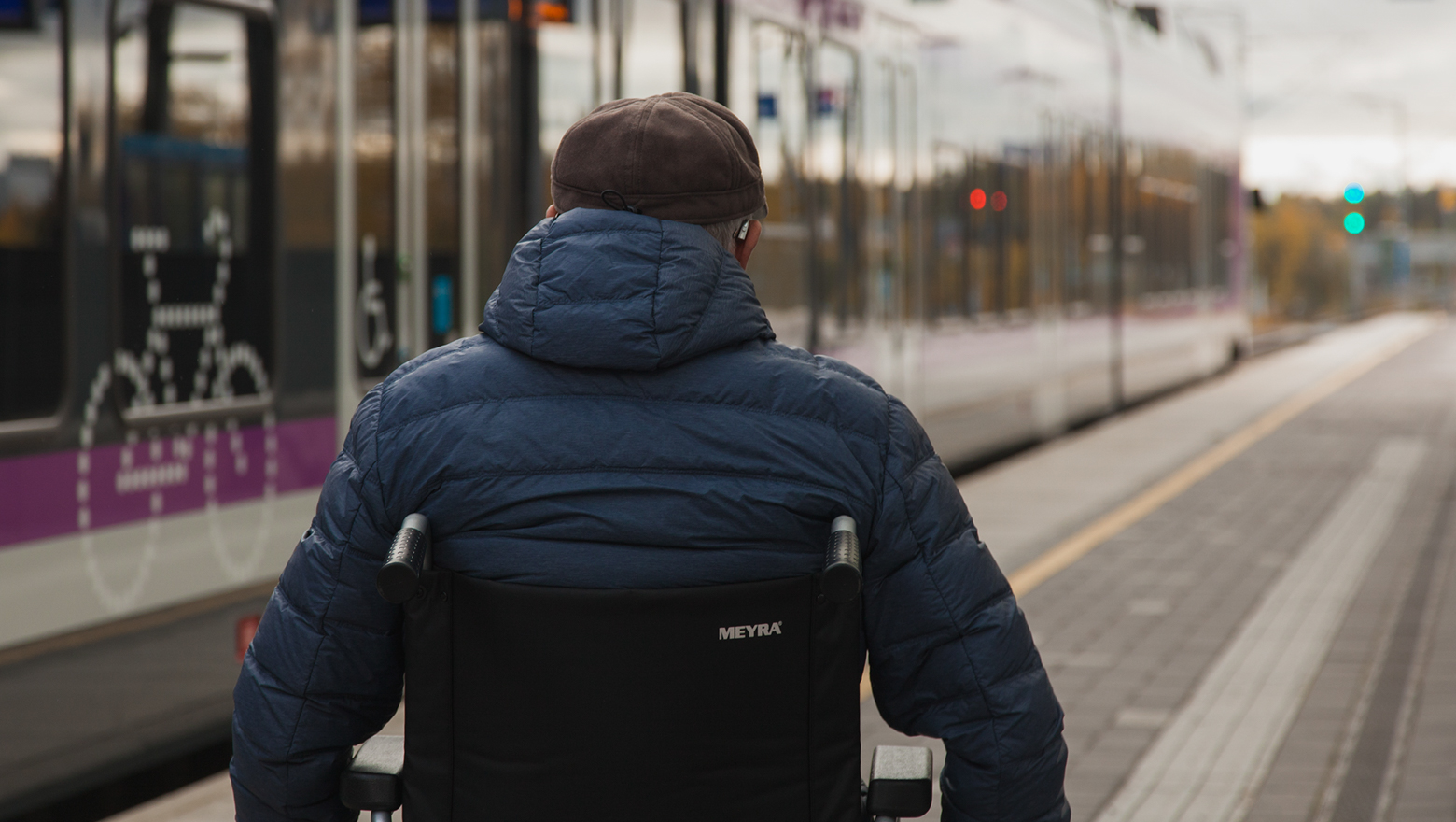 Pyörätuolia käyttävä henkilö asemalaiturilla paikallisjunan vieressä.