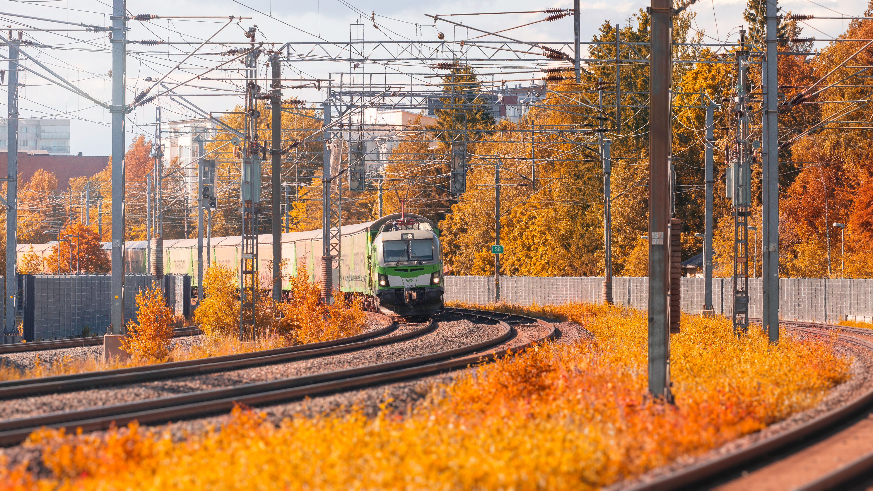 Ruskansävyiset puut ja pensaat junaradan ympärillä, taka-alalta lähestyy juna.