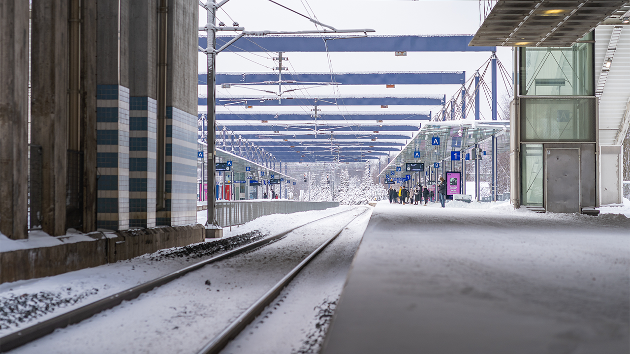 Talvinen kuva Leppävaaran asemalta. Kuvassa junarata ja laituri sekä hissit ja portaat. Laiturilla on ihmisiä odottamassa junaa.