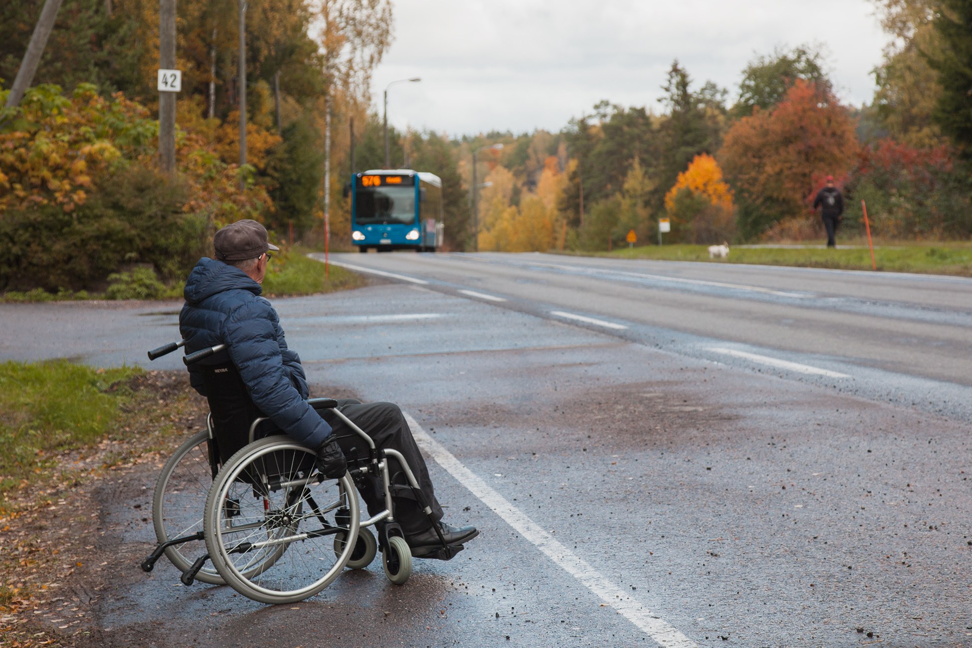 Pyörätuolin käyttäjä odottaa bussia tien varressa.