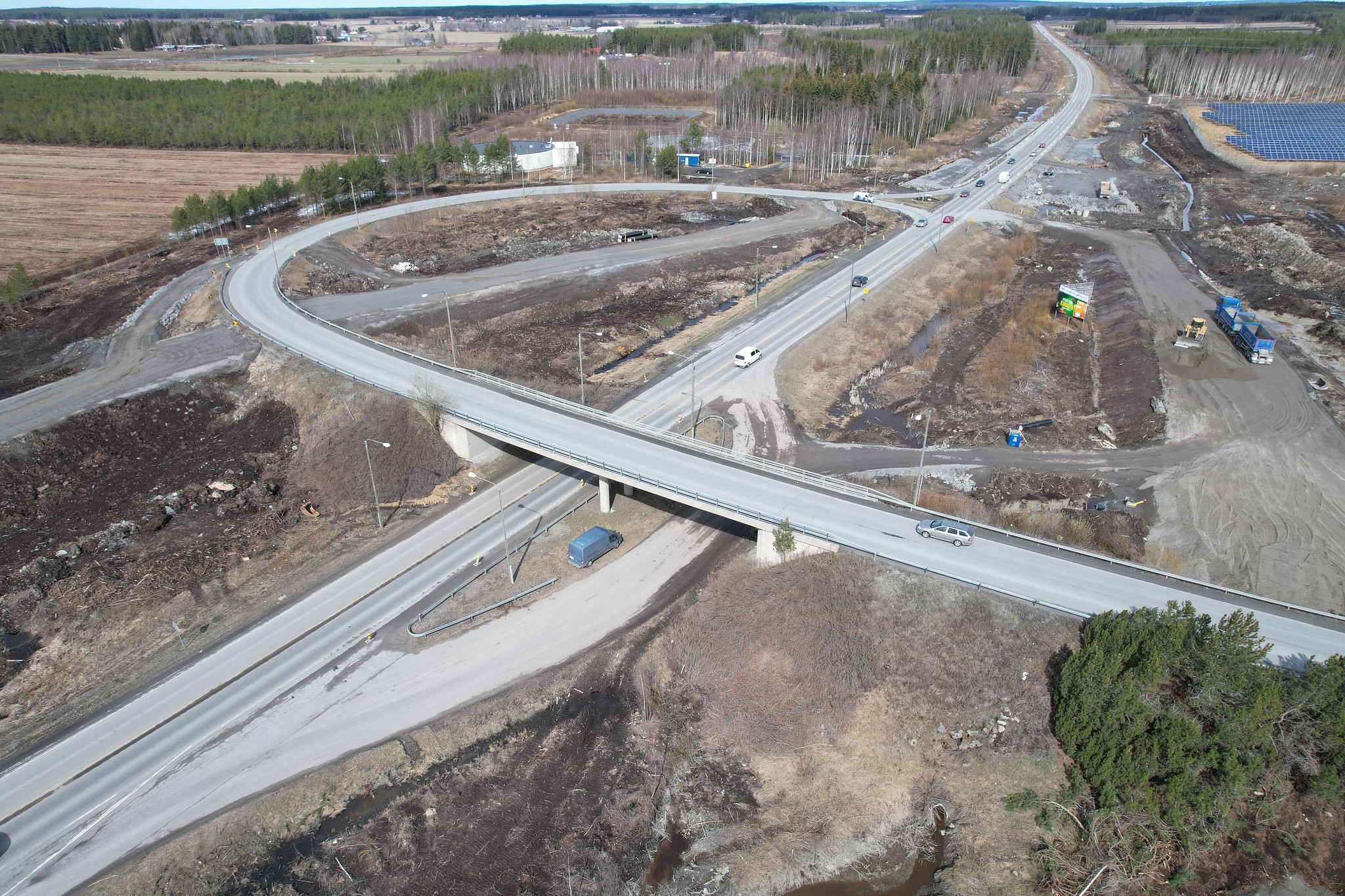 Ilmakuva vastavalmistuneesta eritasoliittymästä. Maaperä on vielä rakennustöiden jäljiltä paljas. Tiellä ajaa autoja, ja taustalla näkyy peltoa, metsää ja aurinkopaneeleita.