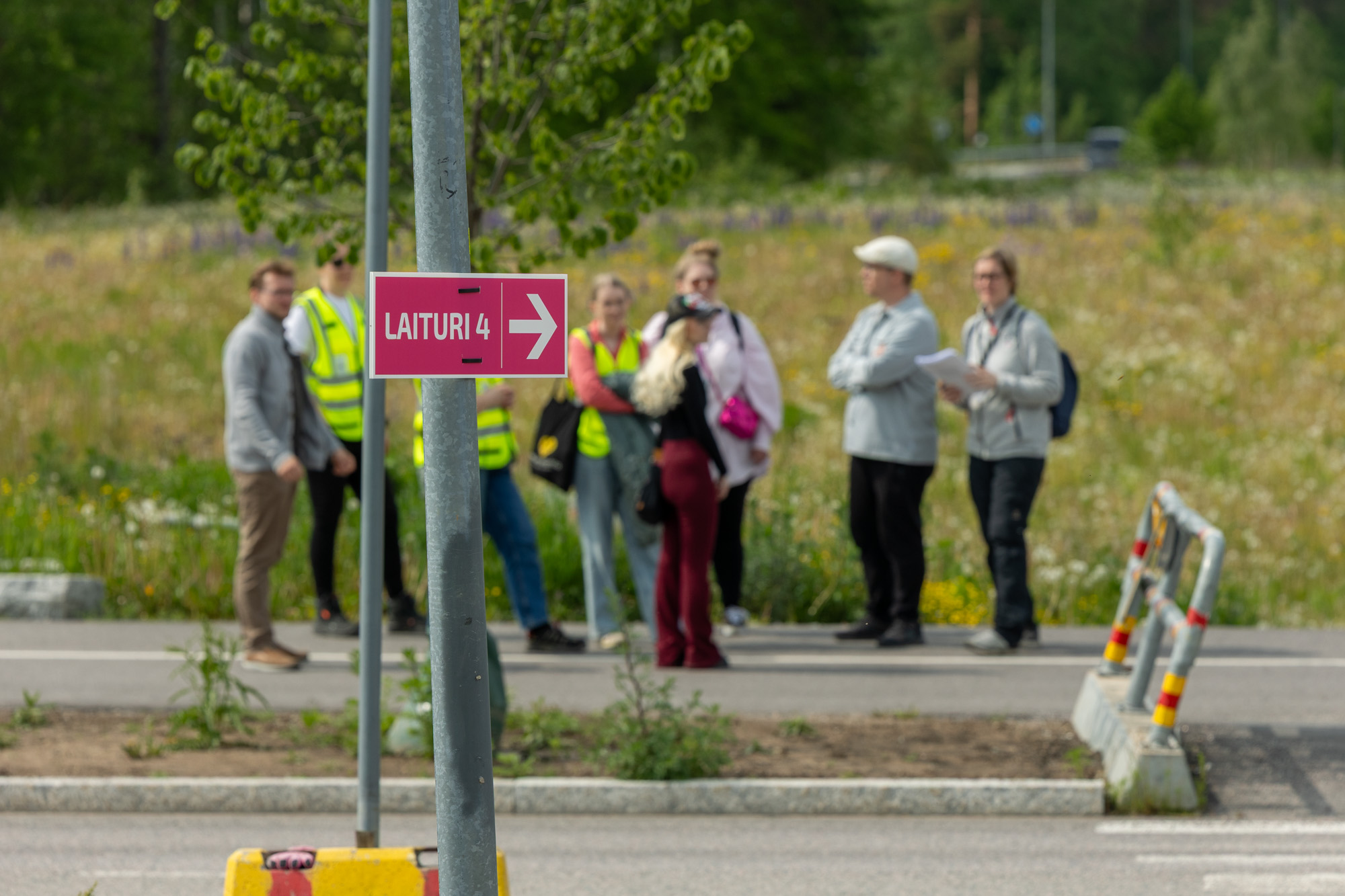 Pinkki kyltti, joka ohjaa laiturille ja taustalla sumeana kansalaistestaajia.