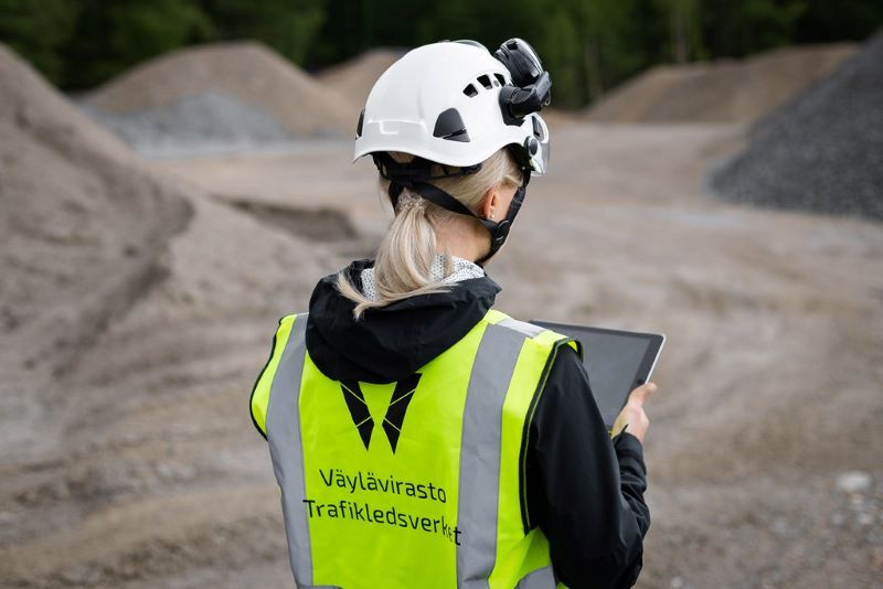 Väyläviraston työntekijä on työmaalla Väyläviraston liivi päällä ja kädessään padi, josta katsoo tietoja.