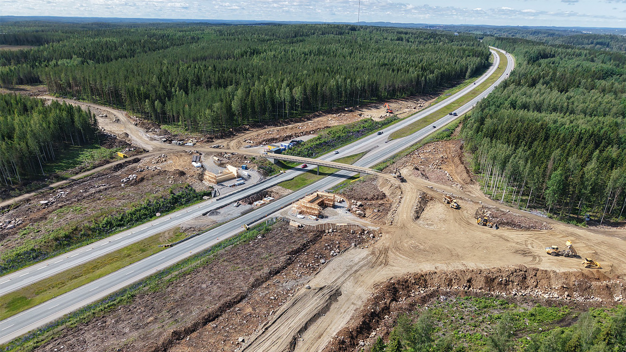 Dronekuvassa näkyy, kuinka eritasoliittymä alkaa hahmottua. Valtatie 3 kulkee vehreän metsän halki ja eritasoliittymän kohdalla tehdään rakennustöitä.