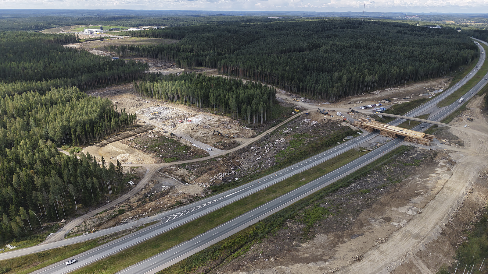 Dronekuvassa valtatie 3 kulkee vihreän metsän halki. Tien varrella näkyy rakenteilla oleva eritasoliittymä- ja pysäköintialue.