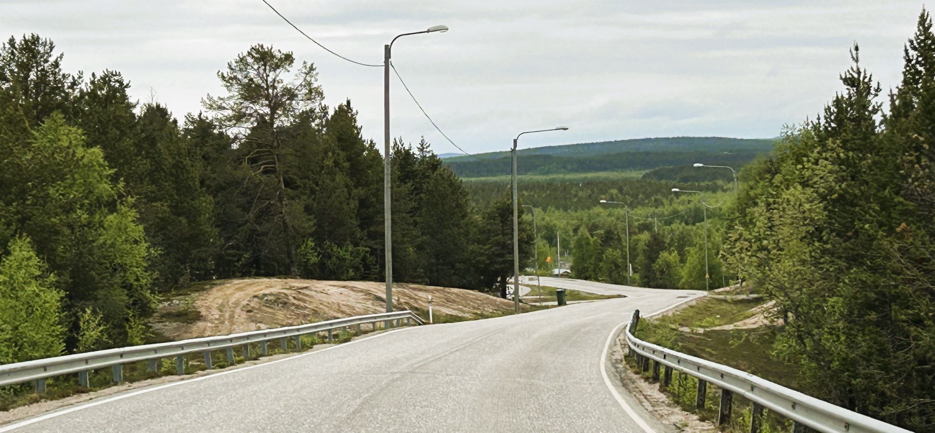 Kuva tiestä valtatie 21 varrella välillä Palojoensuu-Kuttanen. Kuvassa keskellä mutkainen, alamäkeen laskeva tie, jonka varsilla metsää. Taustalla näkyy tunturimaisema.