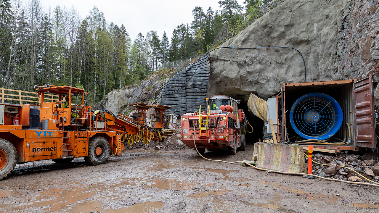 Kuva: Porajumbo on hoitanut työnsä ja on panostuslaitteen vuoro ajaa tunneliin. Tuulettimen avulla räjäytyksen jälkeiset kaasut saadaan imettyä pois tunnelista (oik.).