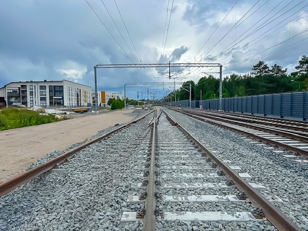 Uusi vaihde käytössä olevien raiteiden ja tulevan raiteen pohjan välissä harmaana kesäpäivänä. Raiteiden alla ratasepeliä, taka-alalla vaaleita kerrostaloja.