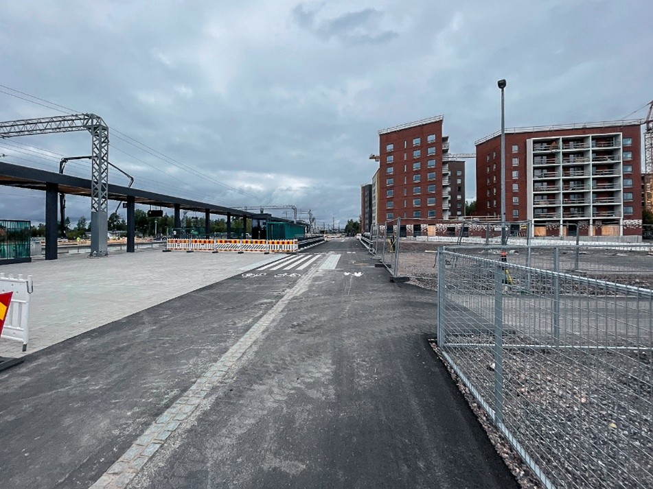 Asfaltoitu katu, jonka keskellä kulkee ohjaava laatoitus. Vasemmalla Ainolan uusi itäinen laituri, oikealla punaisia kerrostaloja ja työmaa-aidoilla rajattuja alueita harmaana syyspäivänä.