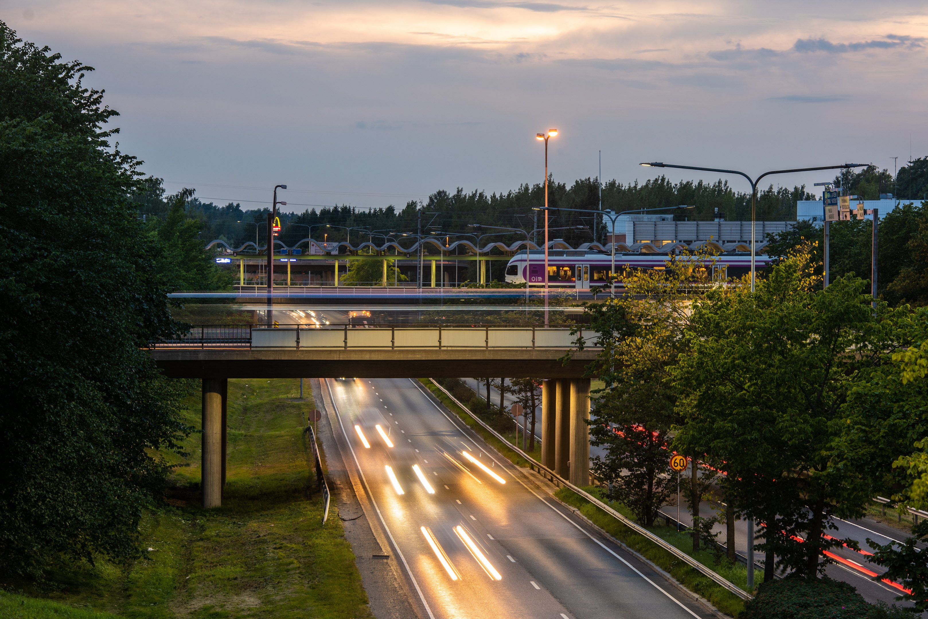 Liikenneympäristöä illalla. Kuvassa tie ja rautatiesilta, jossa juna.