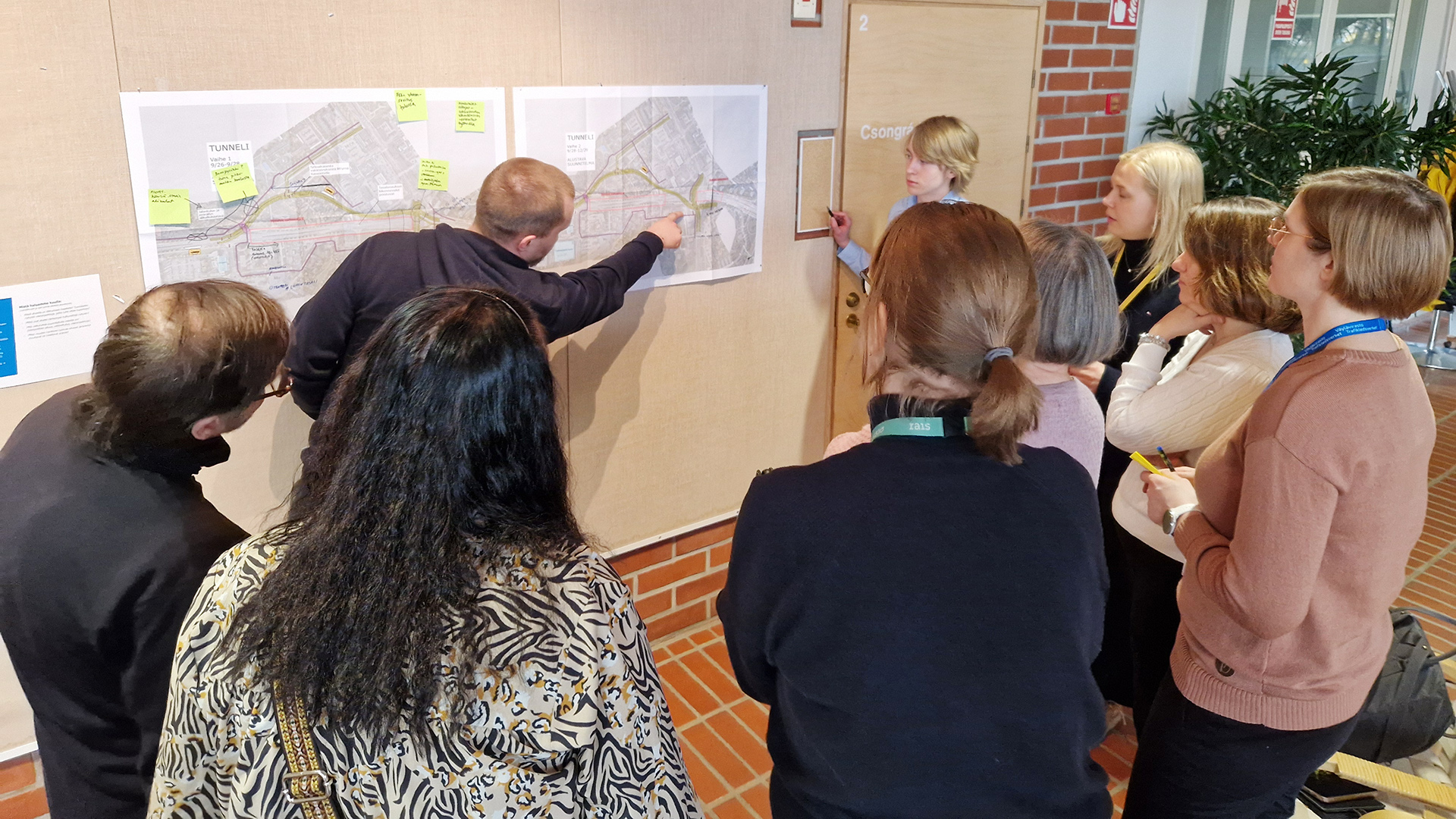 Joukko ihmisiä tutkii seinälle kiinnitettyä karttakuvaa.