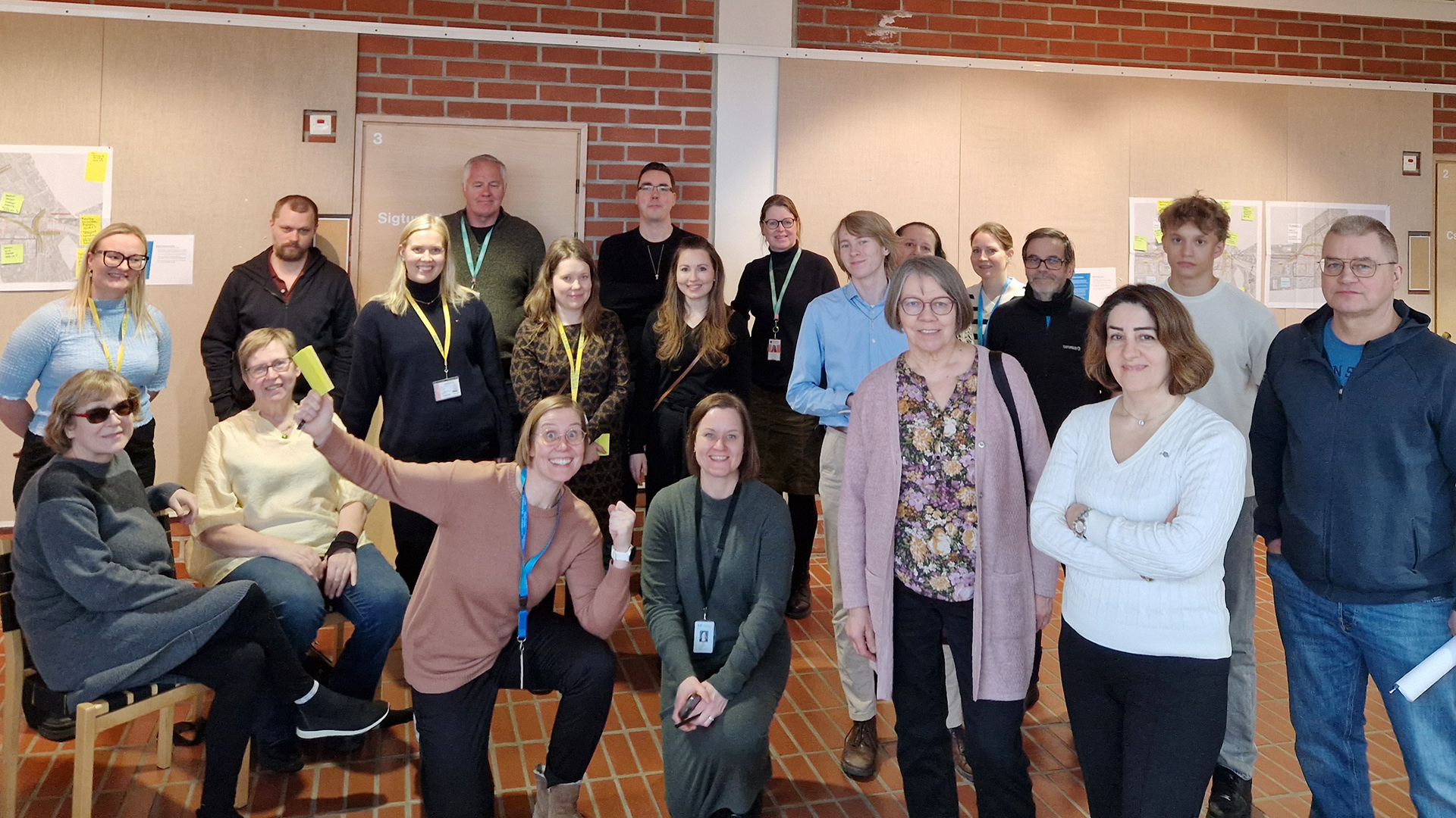 Ryhmäkuvassa joukko eri ikäisiä ihmisiä. Taustalla seinällä tulostettuja karttakuvia, joihin on kirjoitettu käsin kommentteja.