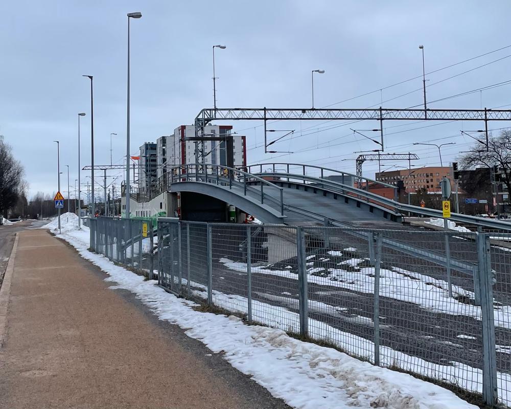 Vasemmalla kulkee hiekkapintainen tie ja oikealla on raitatiealue. Rautatiealueella on kaareva ajoluiska, joka johtaa autojunaan.