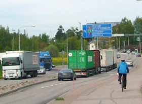 Tiellä kulkee henkilöautoja ja raskasta liikennettä. 