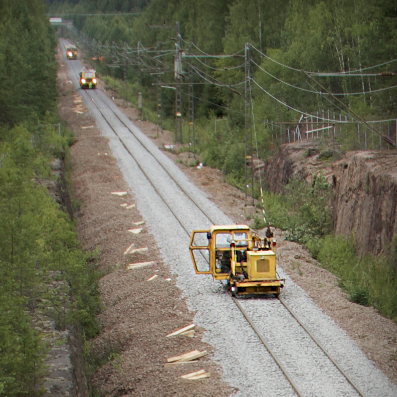 Keltaista pienehkön veturin kokoista humppakonetta seuraa kauempana soravaunu.