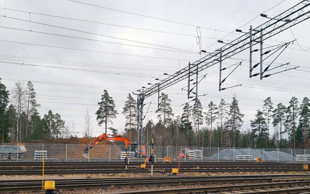 Kuvassa näkyy junarataa ja sen yllä sähköjohtoja. Raiteiden välissä on aita.