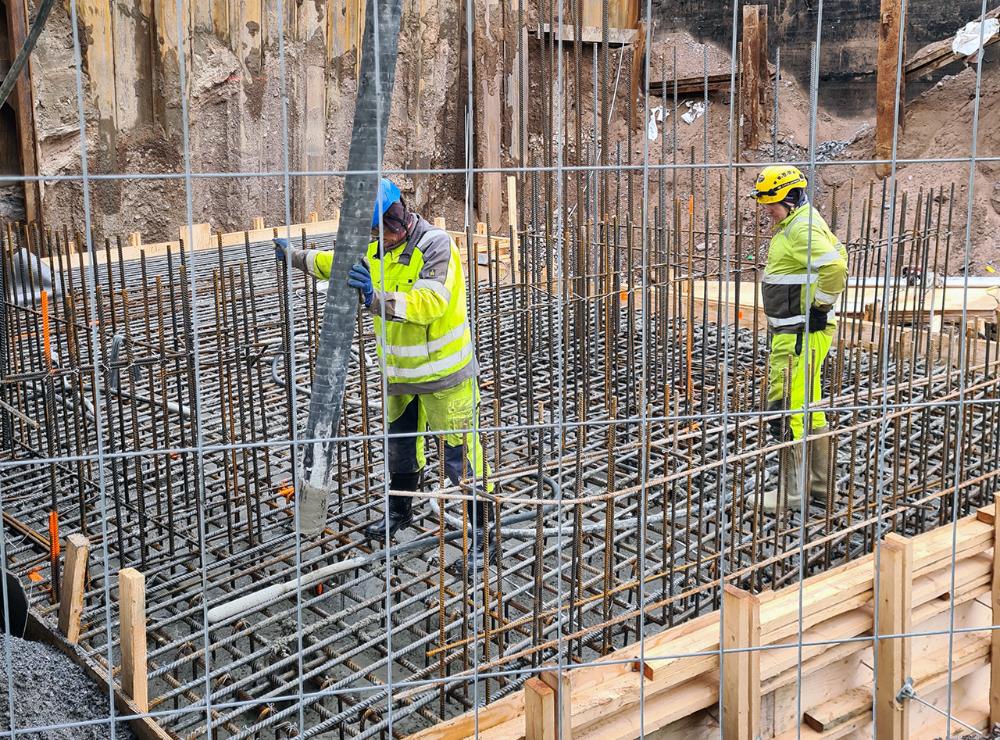 Kuvassa kaksi työmiestä valuttaa betonia muotin päälle.