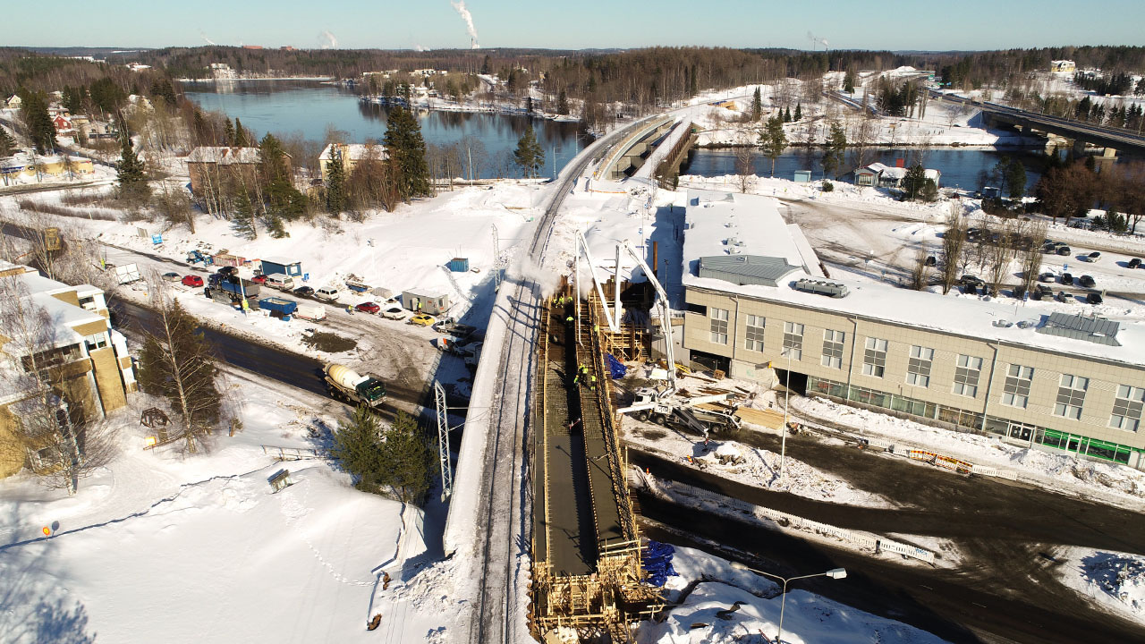 Kuvassa näkyy tie, jonka yllä kulkee silta. Oikealla on iso rakennus.