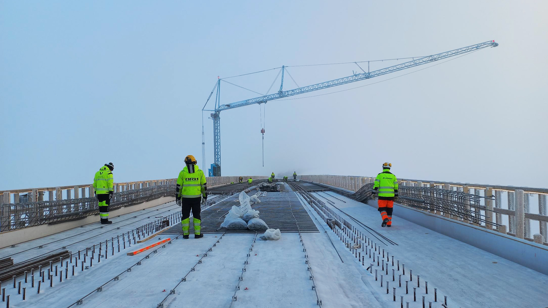 Rakentajia Huikun sillan kannella. Taustalla näkyy nosturin puomi. Maisemaa ei näy sumun takaa.