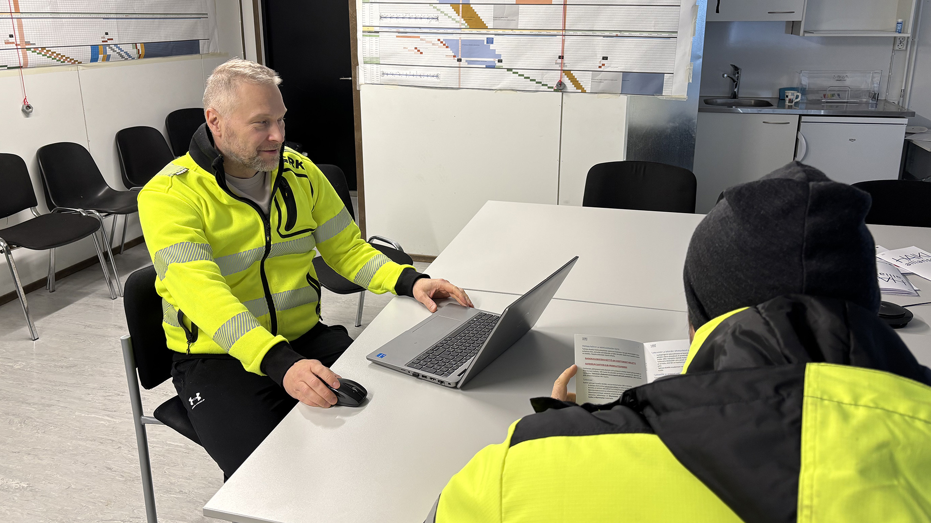 Matti Lievonen käy hankkeen sisältöä läpi perehdytettävän kanssa projektitoimistolla pöydän ääressä.