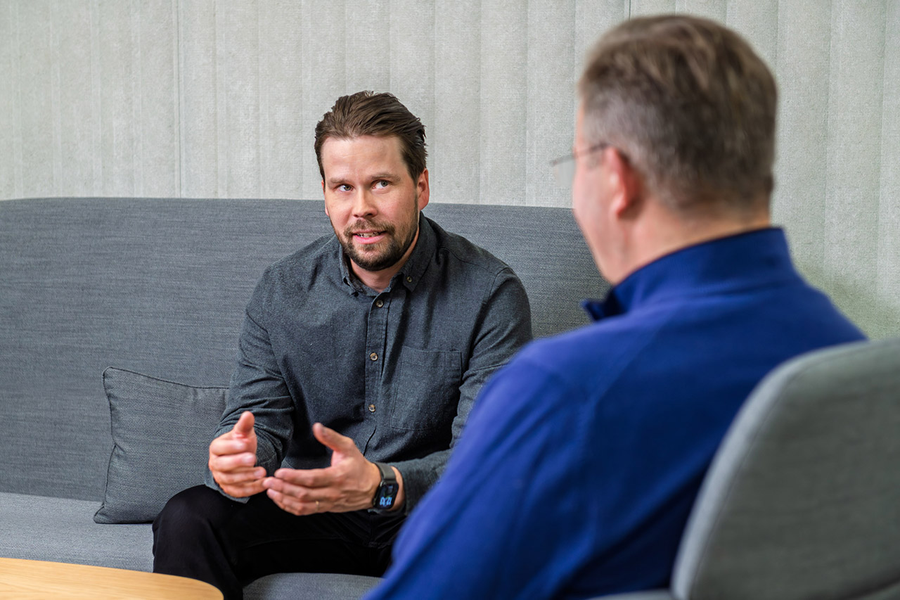 Sohvalla istuva henkilö keskustelee selin olevan henkilön kanssa.