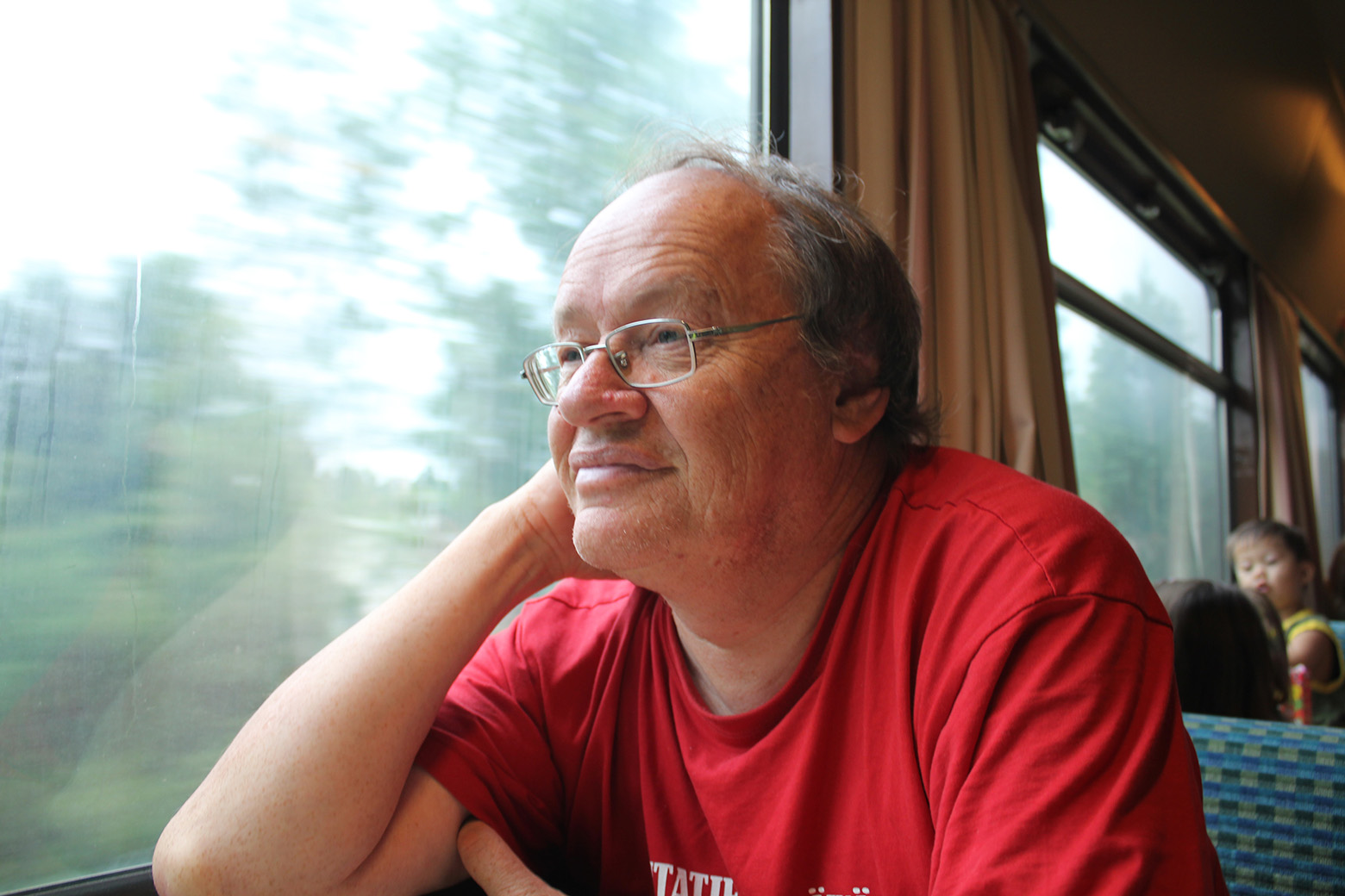 Markku Nummelin istuu junassa punainen paita yllään ja katsoo hymyillen maisemia.