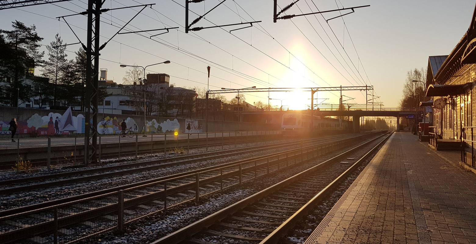 Juna saapuu Hyvinkään asemalle ja taustalla aurinko laskee.