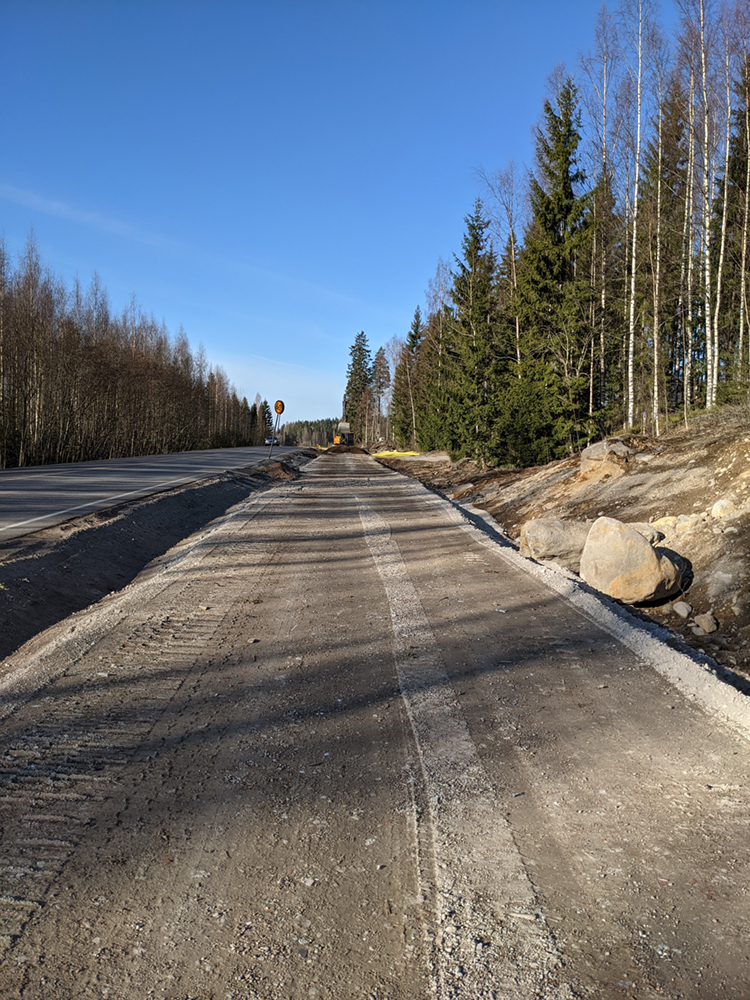 Tasainen, tummanharmaa murskekerros kevyen liikenteen väylän linjalla syksyn maisemassa. Taustalla kaivinkone.