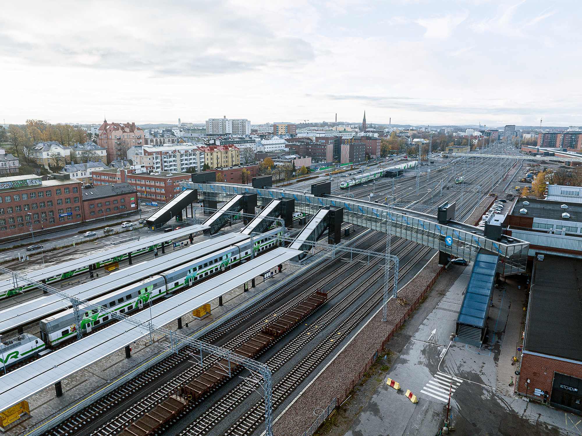 Ilmakuva rautatieasemasta, jossa on useita junia, raiteita ja kävelysilta asemalaitureiden yli. Taustalla näkyy kaupunkimaisema rakennuksineen ja syksyisiä puita.
