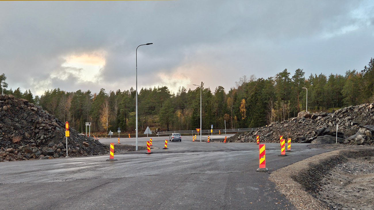 Väg, reflekterande lameller och högar av jordmaterial med sten vid vägkanten.